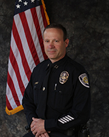 Captain Mike Smith in official BPD Captain's uniform standing to the side of the American flag.