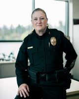 police woman in full dress uniform sitting on a desk in front of a window