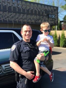 BPD officer holding young boy who is dressed for summer and wearing sunglasses.